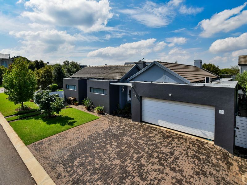 A modern single-story house featuring a dark grey exterior, a paved driveway, a double garage, and a well-maintained front lawn.