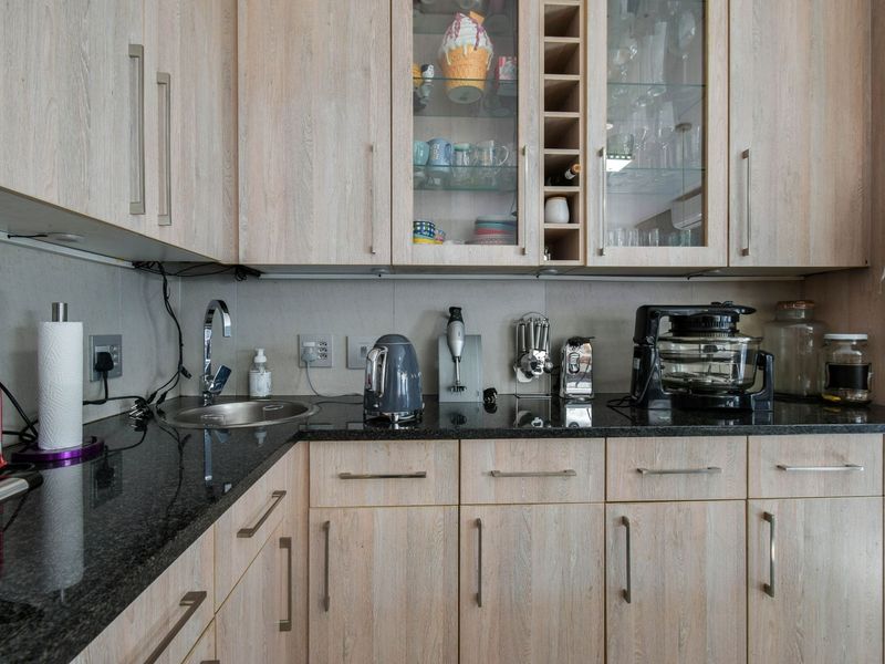 A functional kitchen area featuring light wood-grain cabinetry, dark granite countertops, and a stainless steel sink with integrated storage solutions.