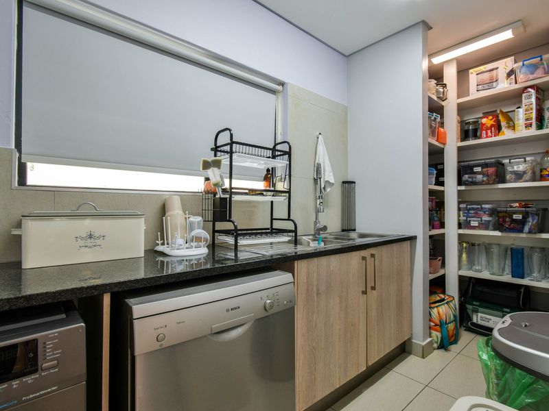 A functional scullery featuring granite countertops, a stainless steel sink, built-in cabinetry, and open shelving for organized storage.