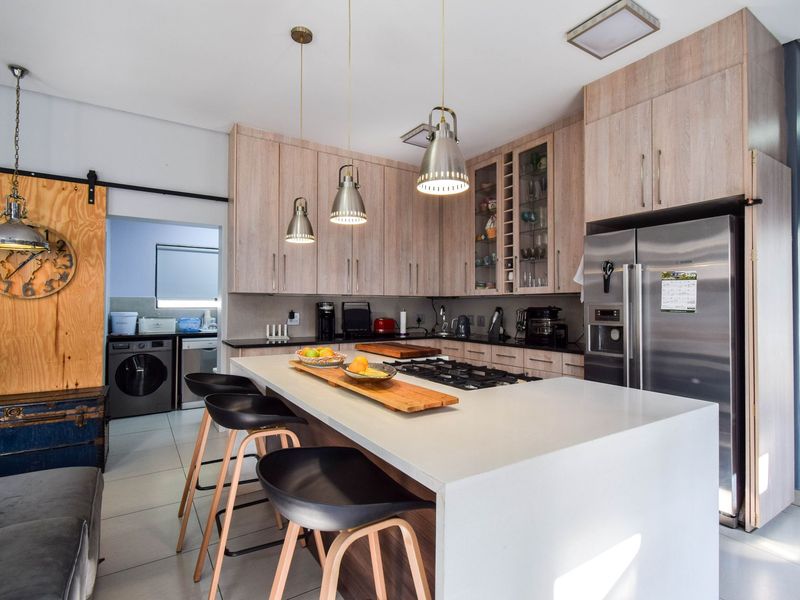 Modern kitchen featuring light wood cabinetry, a large central island with a built-in gas hob, stone countertops, and an adjacent scullery area.