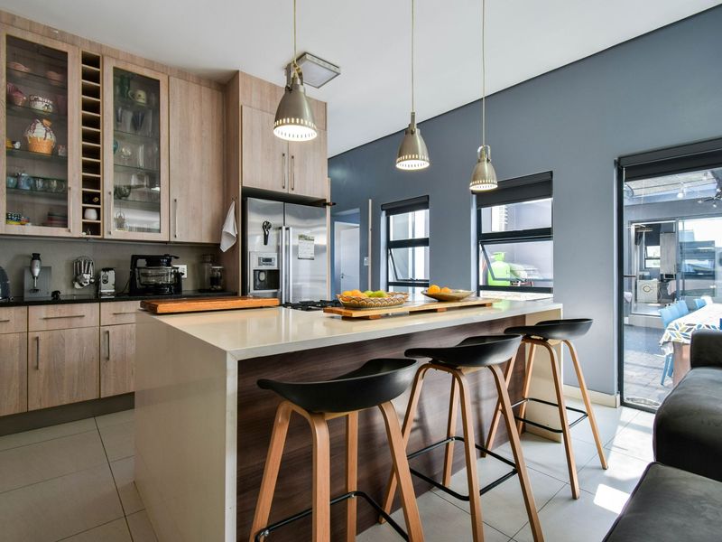 Modern open-plan kitchen featuring light wood cabinetry, a central stone-topped island with breakfast bar seating, and integrated stainless steel appliances.