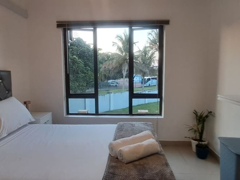 A well-maintained bedroom featuring tiled flooring, aluminium window frames with roller blinds, and a wall-mounted shelf, offering a clean and functional living space.