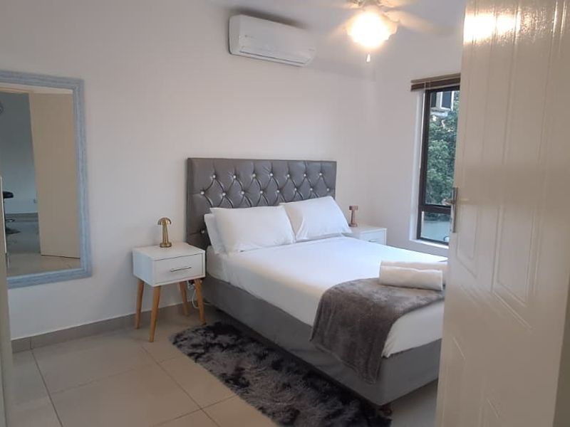 A well-maintained bedroom featuring tiled flooring, a ceiling fan, and a wall-mounted air conditioning unit, offering a comfortable and functional living space.