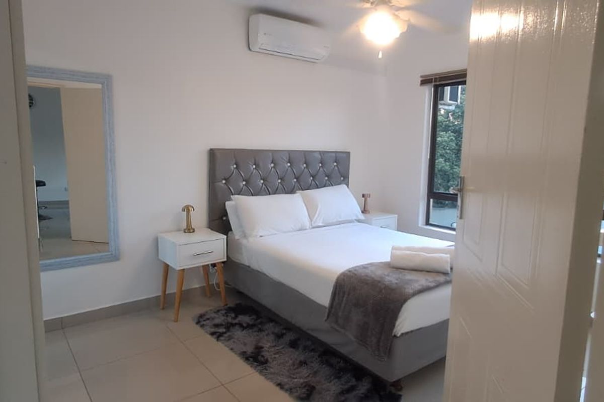 A well-maintained bedroom featuring tiled flooring, a ceiling fan, and a wall-mounted air conditioning unit, offering a comfortable and functional living space.