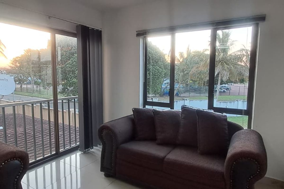 A bright living room featuring large windows and a sliding glass door leading to a balcony, with neutral tiled flooring throughout.