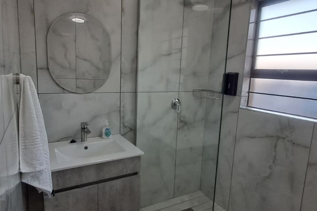 Modern bathroom featuring marble-look wall tiles, a sleek vanity cabinet with basin, and a glass-enclosed shower area.