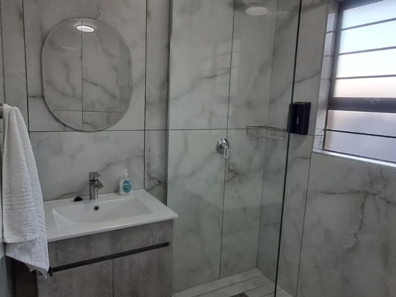 Modern bathroom featuring marble-look wall tiles, a sleek vanity cabinet with basin, and a glass-enclosed shower area.