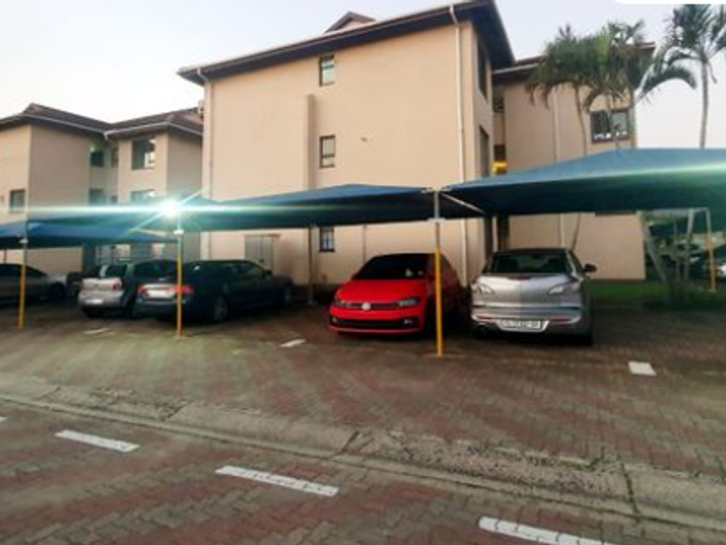 Exterior view of the apartment complex featuring paved parking areas with installed shade cloth carports for residents.