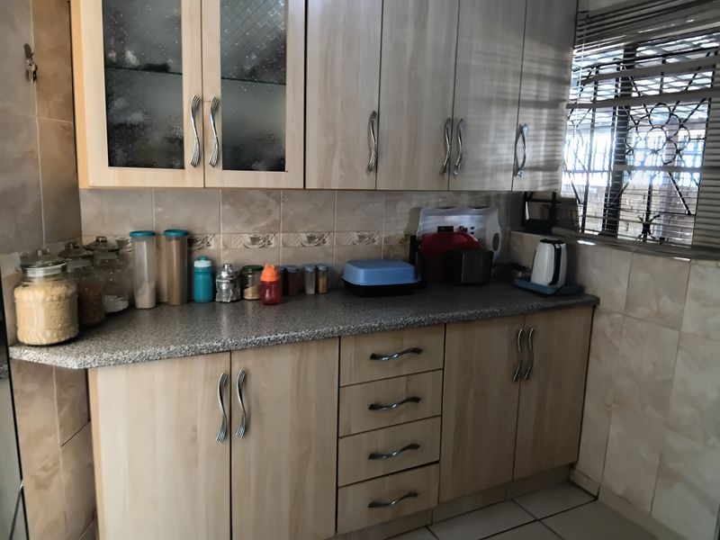 A functional kitchen featuring light wood-tone cabinetry, granite-look laminate countertops, and neutral ceramic wall and floor tiling with security bars on the window.