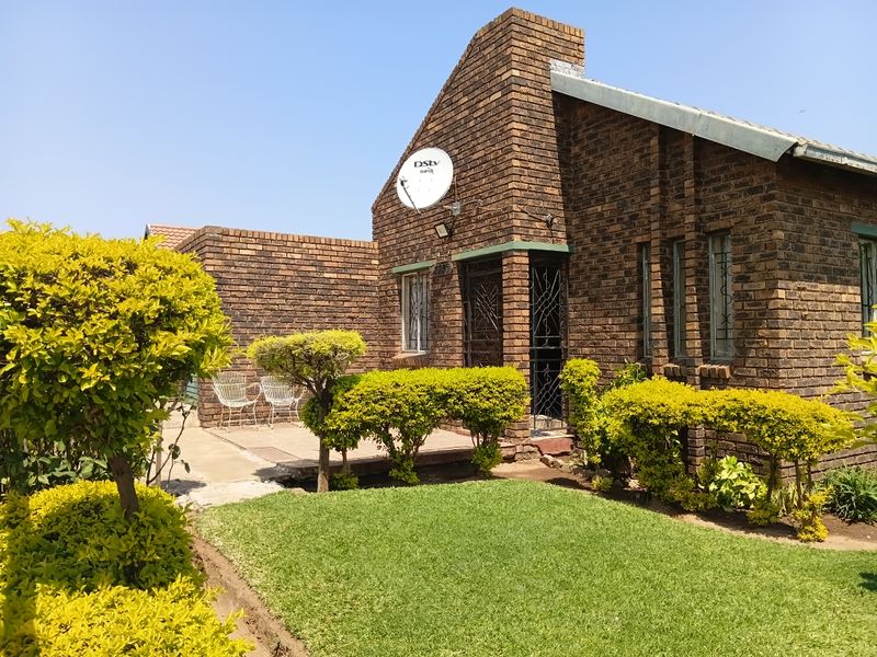 A well-maintained face brick house exterior featuring a paved patio area, established garden, and secure entrance gate.
