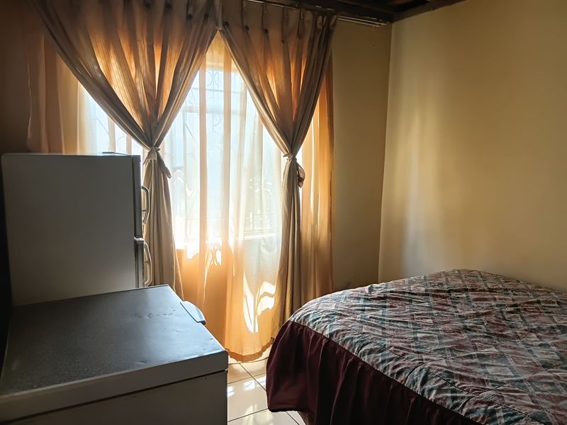 A bedroom featuring tiled flooring and a window fitted with security bars, allowing natural light into the space.