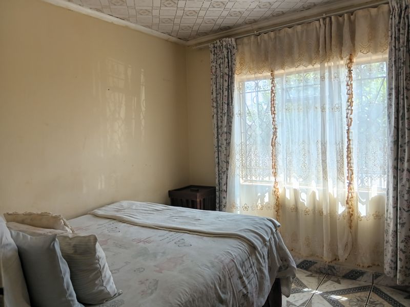 A bedroom featuring tiled flooring, patterned ceiling tiles, and a window fitted with a security gate, offering a dated interior ready for modernization.