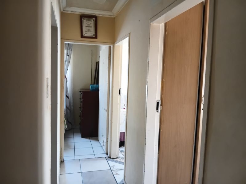 A functional hallway connecting multiple rooms, featuring tiled flooring and standard internal doors, showing signs of wear and requiring cosmetic updates.