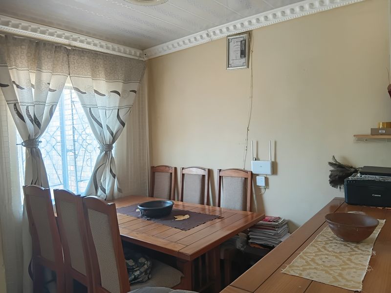 A dining room featuring decorative ceiling cornices, textured ceiling finishes, and security bars on the window, providing a functional space for family meals.
