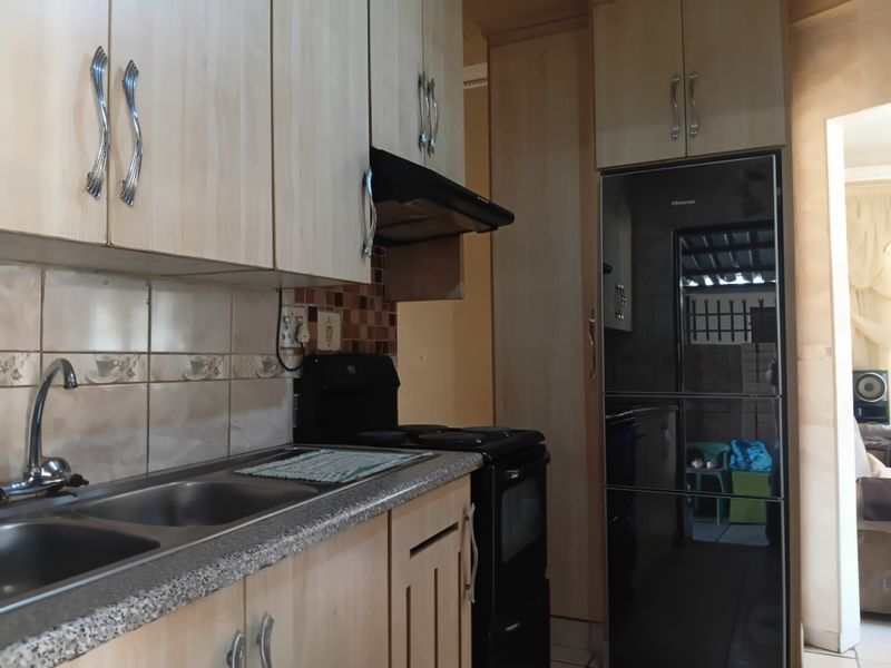 A functional kitchen featuring light wood-finish cabinetry, granite-look countertops, a stainless steel double sink, and integrated cooking appliances.