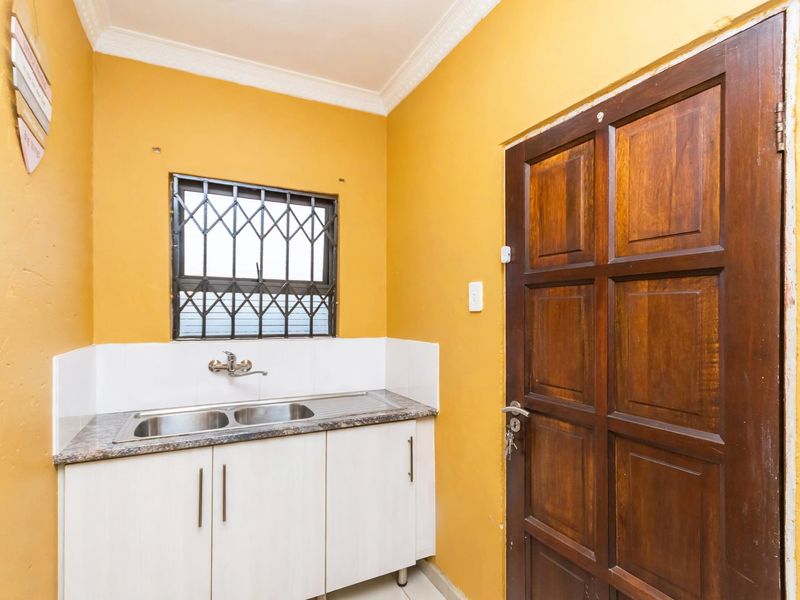 A functional scullery area featuring a double sink, granite countertop, built-in cabinetry, and a secure window with burglar bars.
