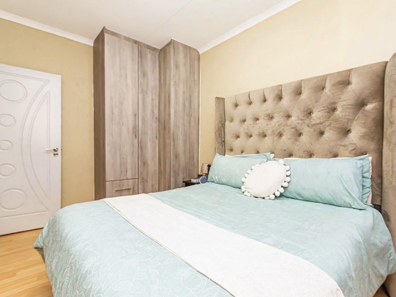 A well-maintained bedroom featuring built-in cupboards, laminate flooring, and a neutral color palette, offering a comfortable and functional living space.