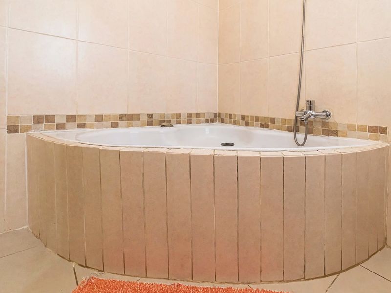 A corner bathtub featuring beige ceramic wall tiles with a decorative mosaic border and a chrome shower mixer.