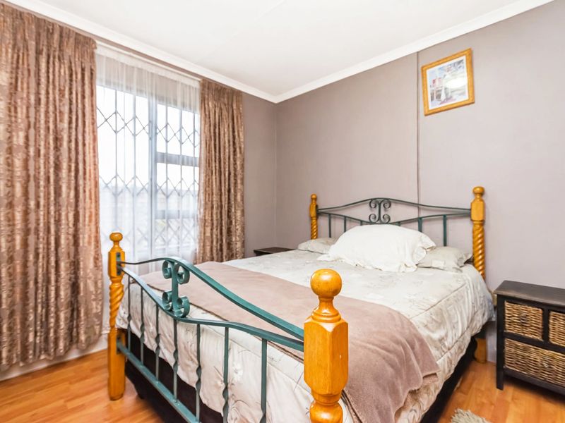 A well-lit bedroom featuring laminate flooring, neutral wall tones, and a secure window with fitted security gate.