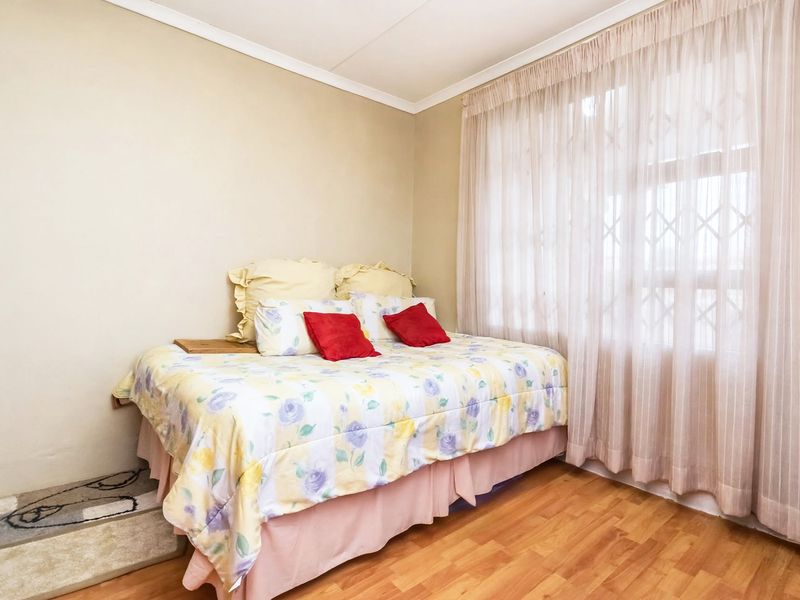 A functional bedroom featuring laminate flooring and a large window fitted with a security gate and curtain tracks.