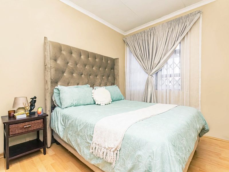 A well-maintained bedroom featuring laminate flooring, neutral wall tones, and a window fitted with a security gate and curtains.
