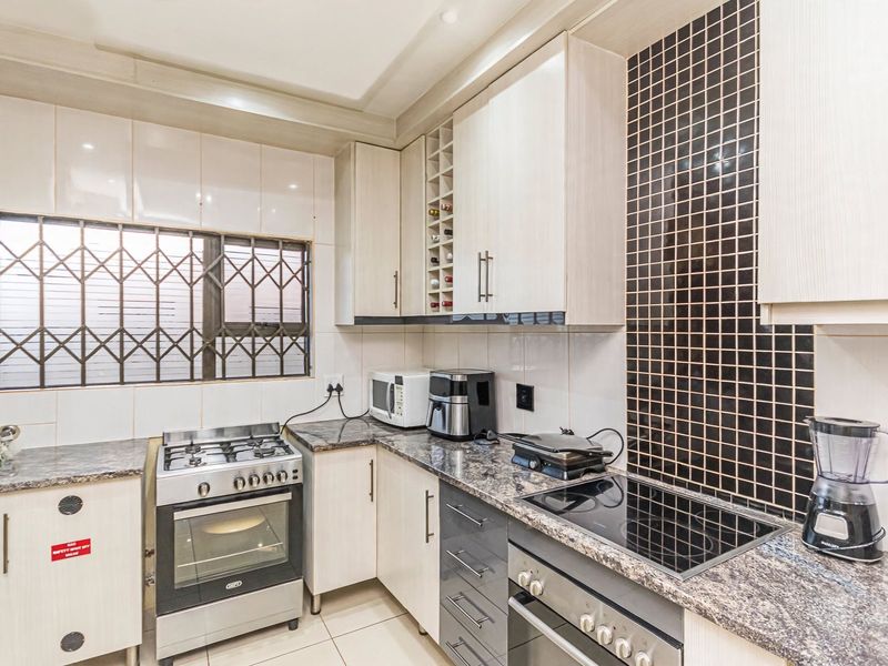 A functional kitchen featuring granite countertops, a combination of gas and electric cooking appliances, built-in cabinetry, and a decorative tiled backsplash.