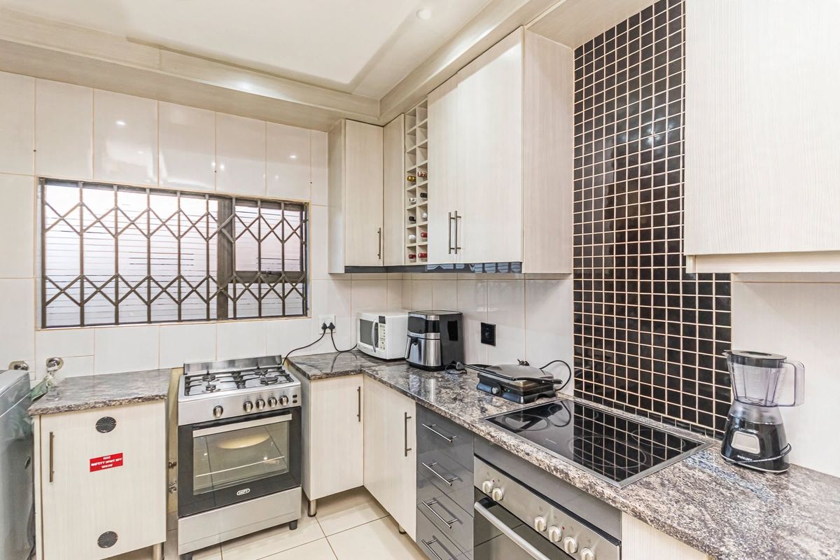 A functional kitchen featuring granite countertops, a combination of gas and electric cooking appliances, built-in cabinetry, and a decorative tiled backsplash.