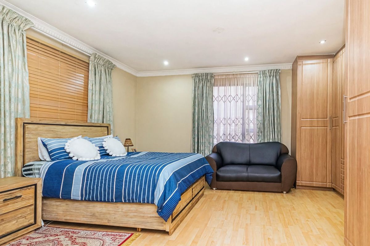 Spacious bedroom featuring light laminate flooring, built-in wooden cupboards, recessed downlighting, and decorative ceiling cornices.