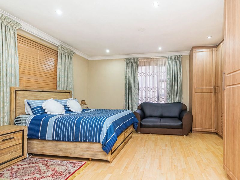 Spacious bedroom featuring light laminate flooring, built-in wooden cupboards, recessed downlighting, and decorative ceiling cornices.