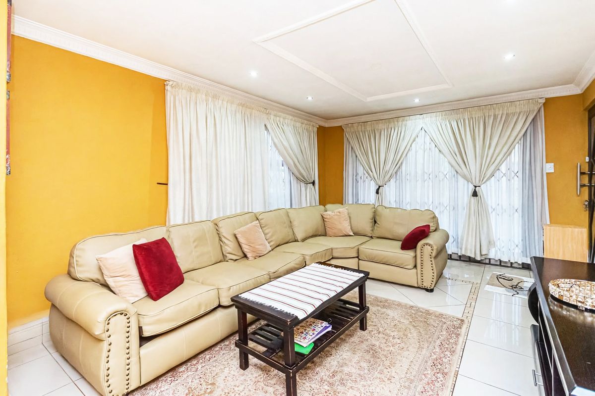 A spacious living room featuring tiled flooring, recessed ceiling lighting, and large sliding glass doors with curtains, providing access to the exterior.