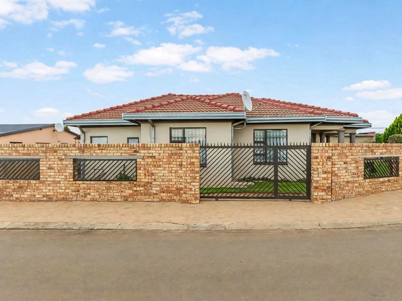 A well-maintained single-story house featuring a face brick boundary wall, secure metal gate, and a tiled roof, situated on a corner plot.