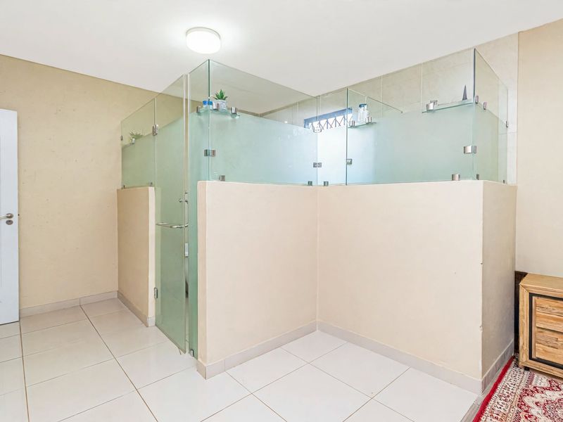 A clean bathroom featuring a modern glass-enclosed shower area with neutral floor tiles and a minimalist design.