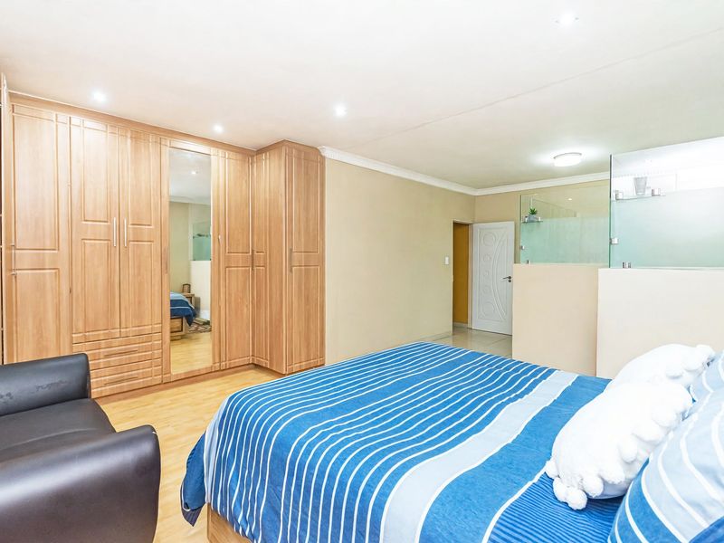 Spacious bedroom featuring extensive built-in wooden cupboards, laminate flooring, recessed lighting, and an open-plan en-suite bathroom area with a glass partition.