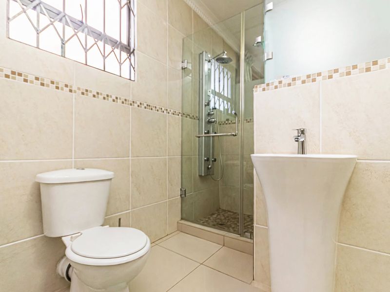 A clean, modern bathroom featuring a pedestal basin, a toilet, and a glass-enclosed shower with a built-in shower panel and tiled finishes.