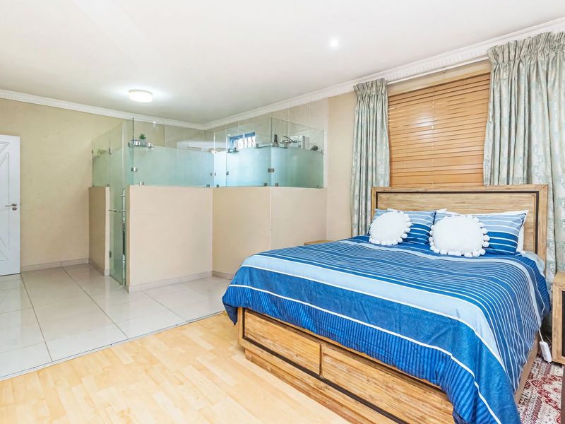 Spacious bedroom featuring an open-plan en-suite glass shower enclosure, tiled and laminate flooring, and neutral wall finishes.