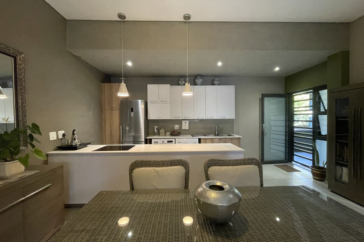 An open-plan kitchen and dining area featuring modern cabinetry, a central island with a built-in hob, and direct access to an outdoor space.