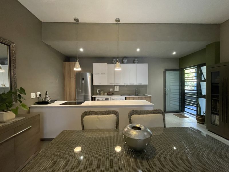 An open-plan kitchen and dining area featuring modern cabinetry, a central island with a built-in hob, and direct access to an outdoor space.