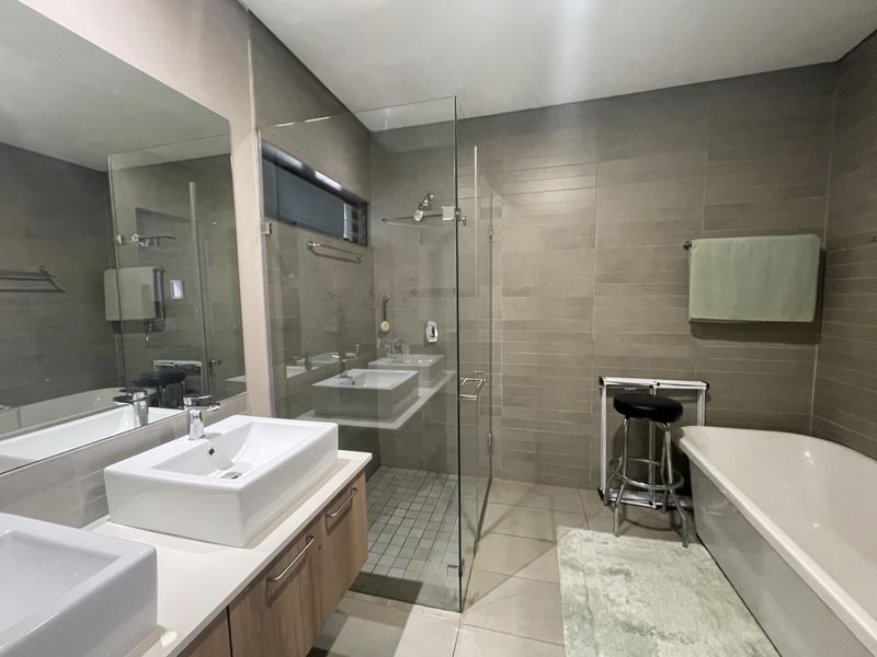 Modern bathroom featuring a double vanity, glass-enclosed shower, and a freestanding bathtub with neutral tiled finishes throughout.
