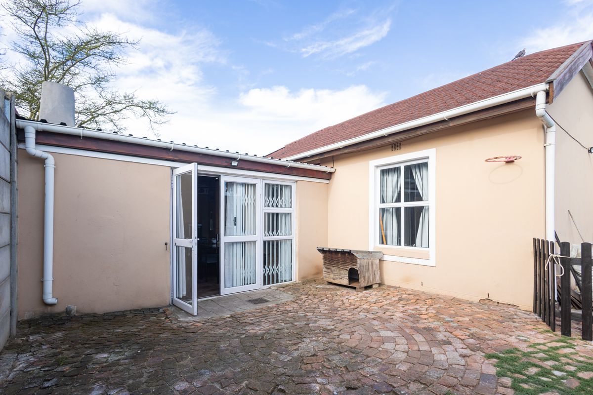 A rear courtyard featuring paved flooring, security-gated glass doors, and exterior access to the main dwelling structure.