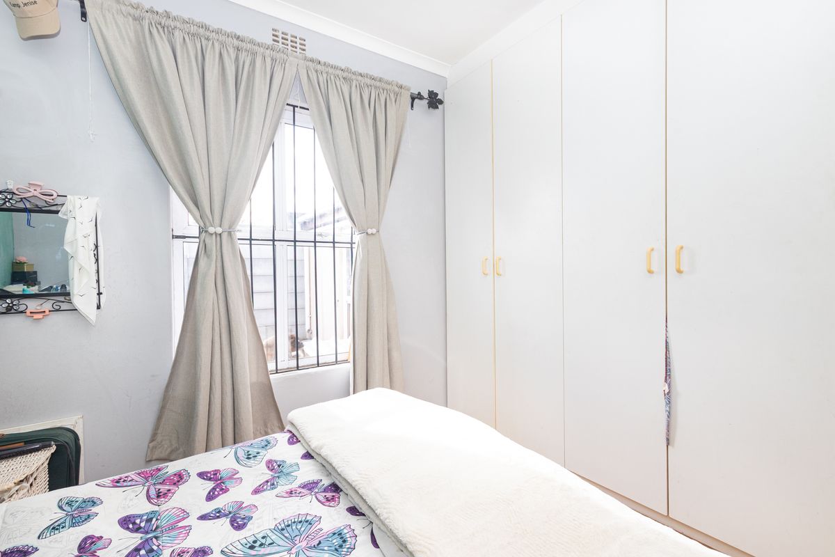 A bedroom featuring built-in cupboards and a window fitted with security bars.