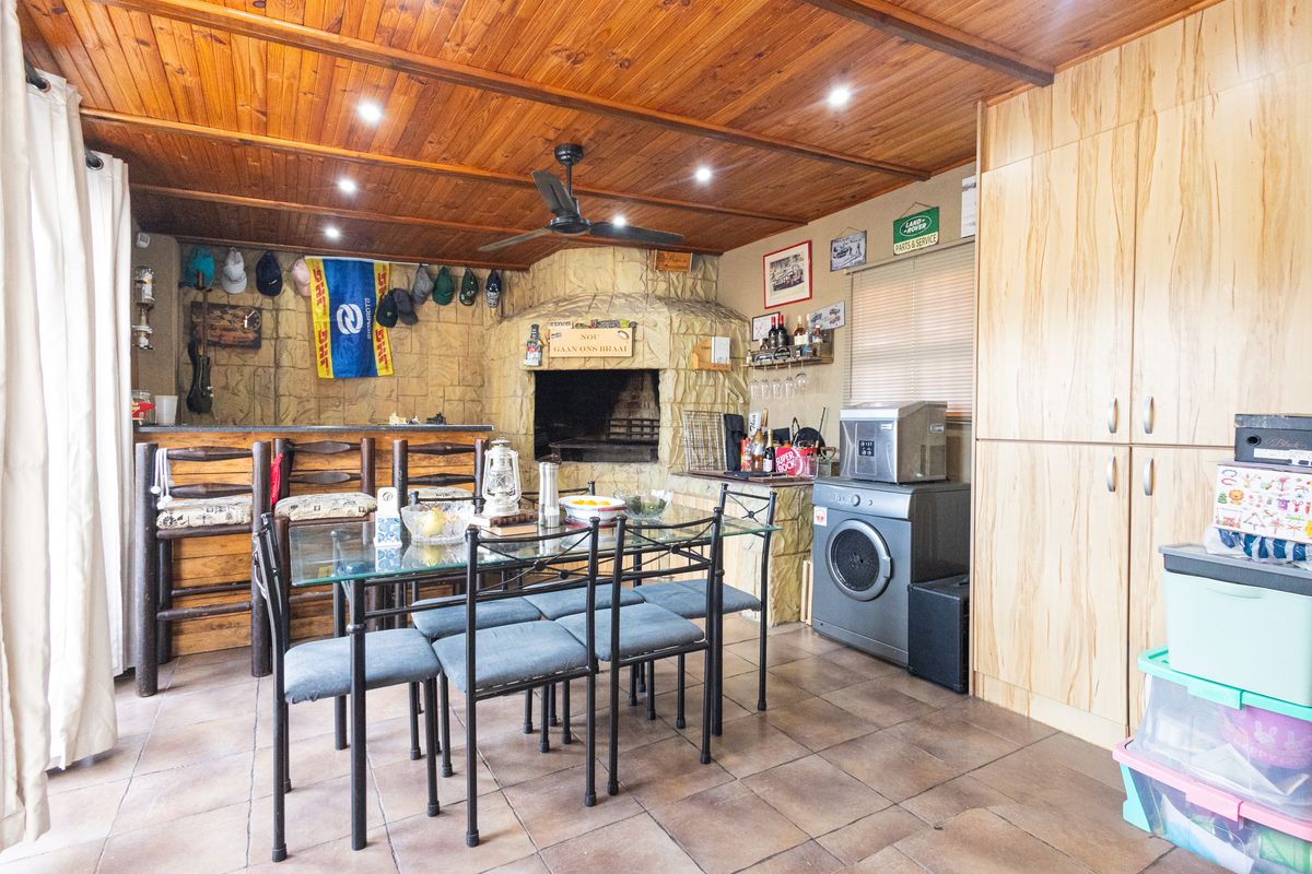 A rustic living area featuring a built-in stone braai, timber-clad ceiling, recessed lighting, and ample built-in storage cabinetry.