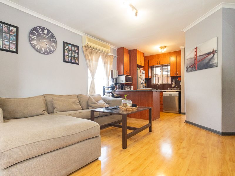 Open-plan living area featuring laminate flooring, a split-system air conditioner, and a functional kitchen with built-in cabinetry and integrated dishwasher.