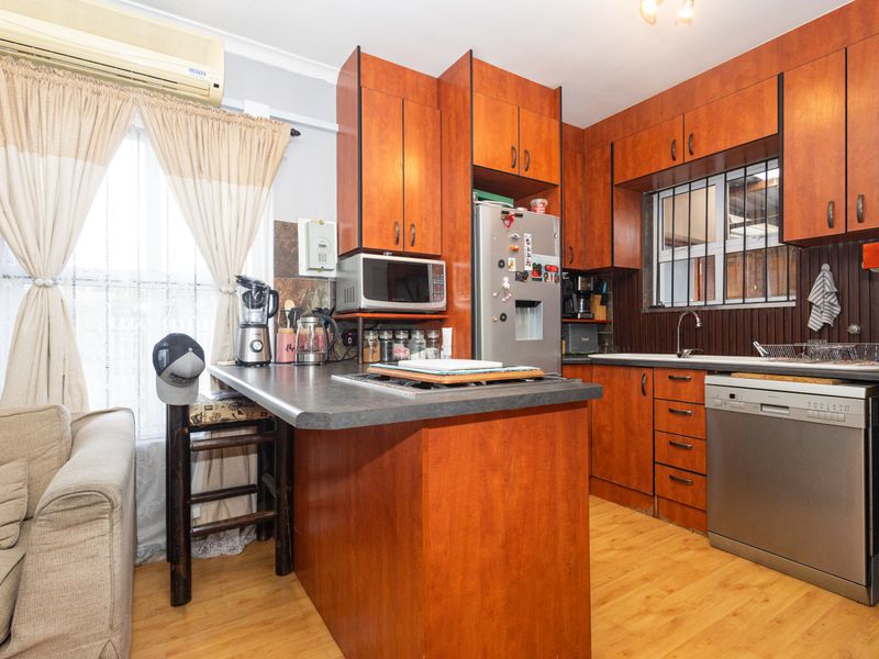 A functional kitchen featuring wood-look laminate cabinetry, integrated appliances, and a breakfast bar, with security bars on the window and wall-mounted air conditioning.