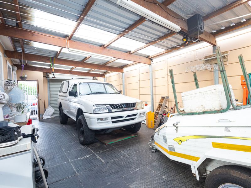 A spacious garage featuring a corrugated roof with timber beams, rubber flooring, and a functional roller door.
