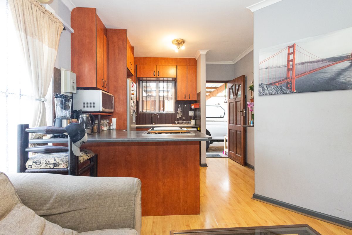 A functional kitchen featuring wooden cabinetry, laminate countertops, and a built-in hob, with direct access to an exterior area through a timber door.