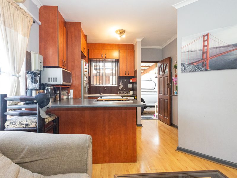 A functional kitchen featuring wooden cabinetry, laminate countertops, and a built-in hob, with direct access to an exterior area through a timber door.