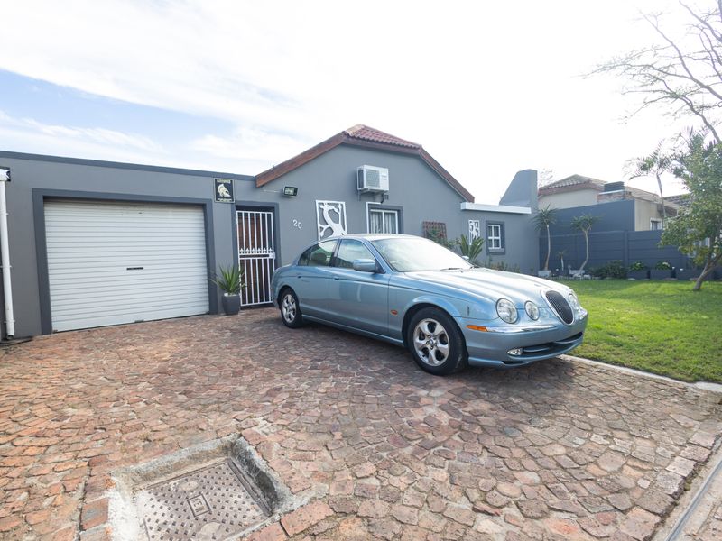 Front elevation of a residential property featuring a paved driveway, single garage, and secure entrance gate.