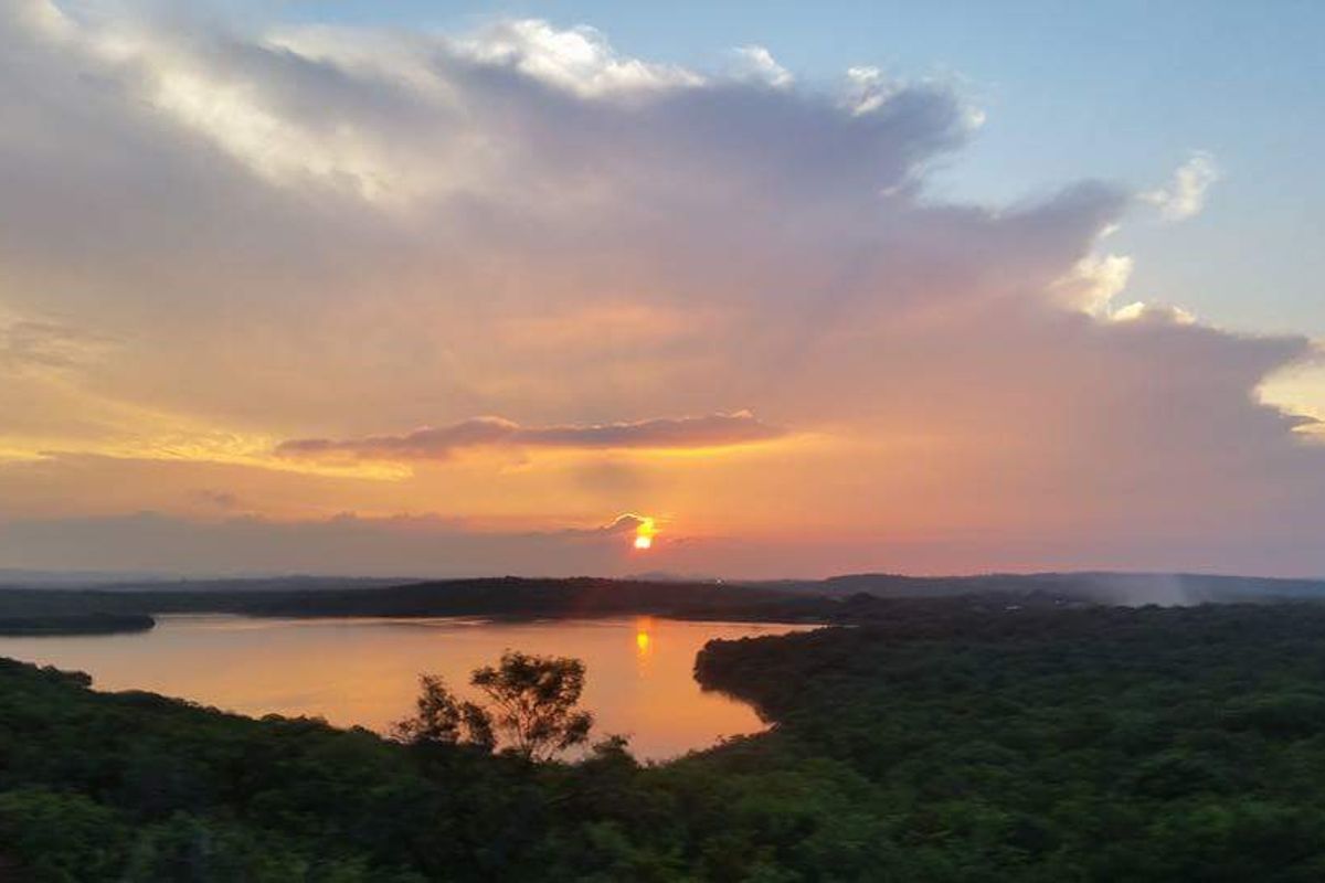 A scenic sunset view overlooking a tranquil lake surrounded by lush natural vegetation.