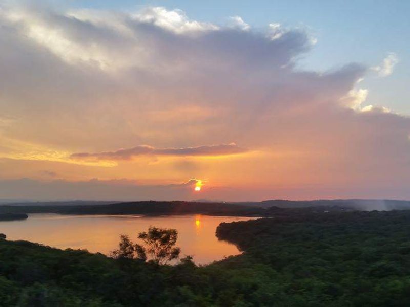 A scenic sunset view overlooking a tranquil lake surrounded by lush natural vegetation.