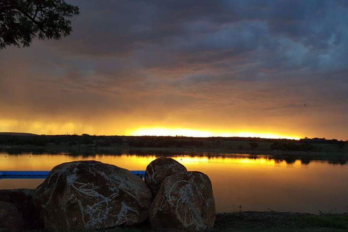 A scenic view of a tranquil lake at sunset, featuring a floating dock and natural rock formations along the shoreline.